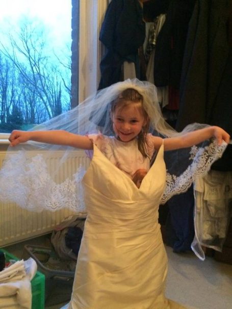 A young girl tries her mum's wedding dress and veil.